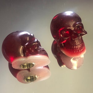 Peut inclure: Deux bouchons de bouteille en forme de crâne en verre rouge avec une finition scintillante. Les bouchons sont creux et ont un trou au fond pour insérer une bouteille.