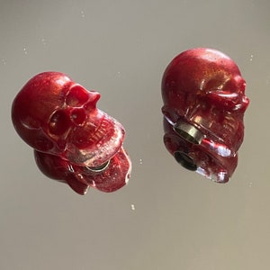 Peut inclure: Deux bouchons de bouteille en forme de crâne rouge avec une finition métallique. Les bouchons ont un petit trou au fond pour insérer une bouteille.