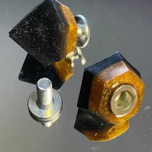May include: Two black and gold resin drawer pulls with a geometric shape and a silver screw.