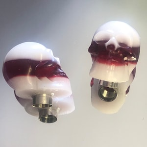 Peut inclure: Deux bouchons de bouteille en forme de crâne rayés de blanc et de rouge avec une base filetée argentée.