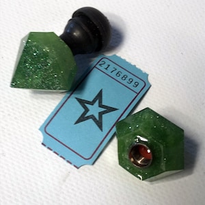 Può includere: Due tappi per bottiglie in resina verde scintillante, sfaccettati, con un pomo nero in cima. I tappi sono su un biglietto blu con il numero 2176899 e una stella nera.
