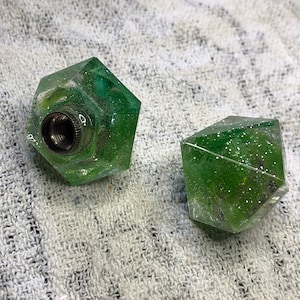 May include: Two green, faceted, resin dice with silver glitter. The dice are translucent and have a shiny finish.