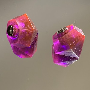 Peut inclure: Deux bouchons de bouteille en verre facetté, de couleur violette et orange, avec un dessus en métal argenté.