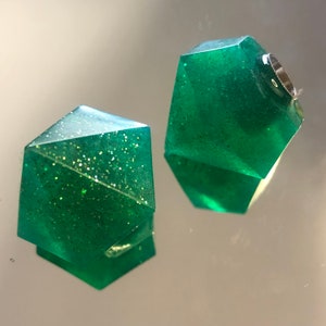 May include: Two green, glittery, geometric resin ornaments. The ornaments are shaped like a diamond with multiple facets.
