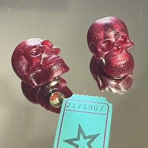 Peut inclure: Deux bouchons de bouteille en forme de crâne rouge pailleté. Les bouchons sont en résine transparente avec une finition pailletée rouge. Les crânes ont un design détaillé avec une mâchoire et des orbites saillantes. Les bouchons sont un ajout amusant et festif à n'importe quel bar à domicile.