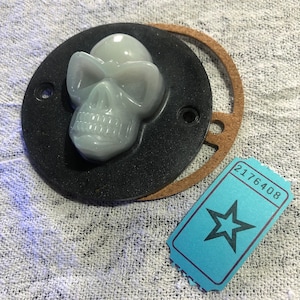 May include: A white skull with sunglasses, moulded in plastic, is mounted on a black circular base with a brown leather ring. The skull is a decorative item.