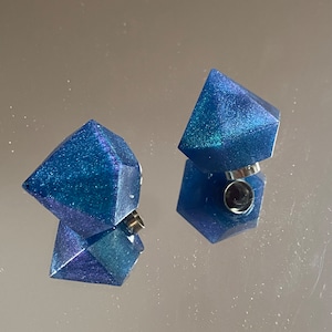 Può includere: Due orecchini a forma di diamante blu e verde con glitter e perni d'argento.