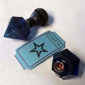 May include: Two blue and black glass bottle stoppers with a blue ticket with a star and the number 2176976.