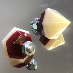 May include: Two decorative, geometric, resin knobs with a red and white color scheme. The knobs have a metal screw attachment.