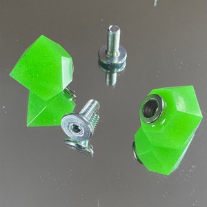 Peut inclure: Trois pièces en résine de forme géométrique, vertes et scintillantes, avec des bouchons à vis en métal argenté. Les pièces en résine ont la forme d'une pyramide avec une base plate et un sommet pointu.