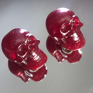 Peut inclure: Deux bouchons de bouteille en forme de crâne rouge pailleté.