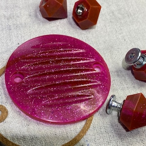 May include: A pink, round, glittery, plastic cover with a ribbed design. The cover has two holes on the side.