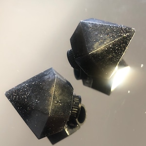 May include: Two black diamond-shaped bottle stoppers with a glittery finish. The stoppers have a threaded base for attaching to a bottle.