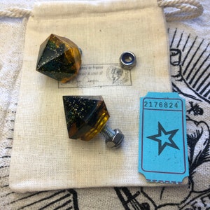 May include: Two gold and black glitter diamond-shaped drawer pulls with silver hardware. The pulls are on a white fabric background.