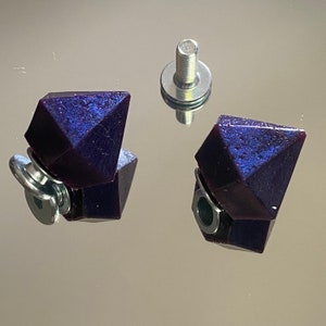 Könnte beinhalten: Zwei dunkelviolette, diamantförmige Harzembellen mit silbernen Schraubsockeln.