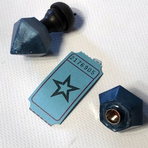 May include: Two blue, faceted, glass bottle stoppers with a black wooden knob on top. One stopper has a ticket with the number 2176905 and a black star printed on it.