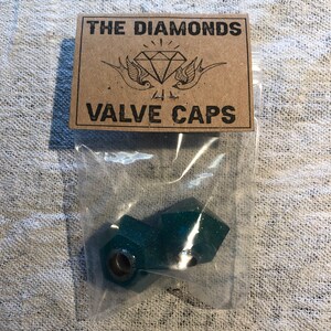 Può includere: Due tappi per valvole di colore verde turchese con glitter in un sacchetto di plastica trasparente con un'etichetta di carta marrone che recita "THE DIAMONDS VALVE CAPS".