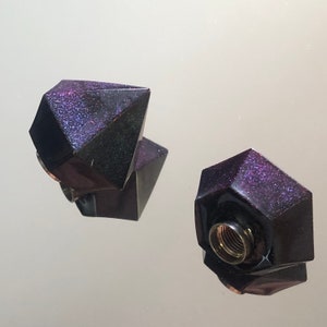 Peut inclure: Deux bouchons de bouteille géométriques de couleur violet foncé avec une finition scintillante.