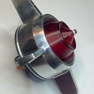 Könnte beinhalten: Ein silbernes Metall-Rücklicht mit roter Linse und einer spitzen Spitze. Das Rücklicht hat vier Flügel, die sich vom Hauptkörper erstrecken.