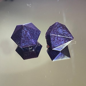 Könnte beinhalten: Zwei dunkelviolette, irisierende, geometrisch geformte Ohrringe aus Harz. Die Ohrringe sind diamantförmig mit mehreren Facetten.