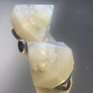 May include: Two clear, white, resin dice with a glittery finish. The dice are shaped like a diamond and have a silver metal base.