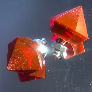 Puede incluir: Dos formas geométricas rojas y brillantes con cierres metálicos plateados. Las formas están conectadas entre sí.