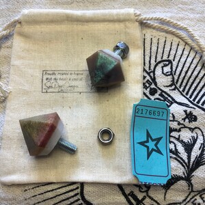 Peut inclure: Deux petites poignées de tiroir en résine de forme géométrique et multicolores avec un matériel métallique argenté. Les poignées sont sur un fond de tissu blanc avec un petit billet bleu qui dit "2176697".