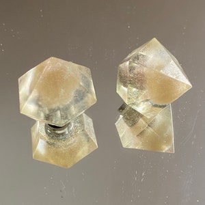 Può includere: Due pomelli per porte in vetro trasparente con forma geometrica e base in metallo argentato.