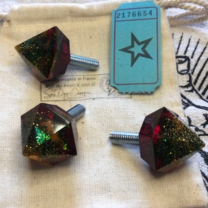 May include: Three diamond-shaped drawer pulls with gold and green glitter embedded in red resin. Each pull has a silver screw.
