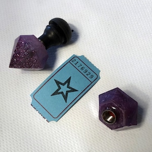 May include: A purple, glitter-filled, diamond-shaped object with a black handle, a small purple hexagonal object, and a blue ticket with a star and the number 2176929.