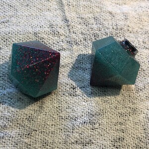 Può includere: Due ornamenti geometrici multi-sfaccettati e scintillanti. Uno è verde acqua e rosso, l'altro è verde acqua e nero.