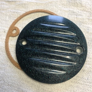 May include: A round, black, metal cover with a textured, ribbed surface and a glittery finish. The cover has two holes on the side.