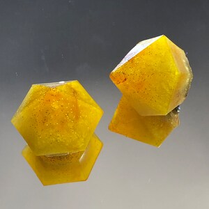 Può includere: Due forme geometriche gialle e scintillanti. Le forme sono di dimensioni simili e hanno un design a stella.