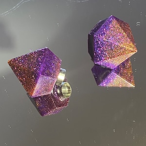 Può includere: Due tappi per le orecchie in resina a forma di diamante, di colore viola e oro glitterato, con un anello in metallo argentato su uno dei tappi.