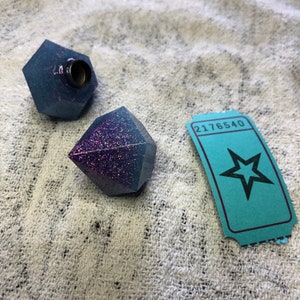 Può includere: Due forme di diamante in resina blu e viola con glitter, con un biglietto a forma di stella con il numero 2176540 stampato.