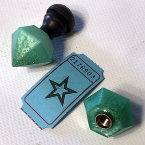 May include: Two green, faceted, diamond-shaped bottle stoppers with black tops. One stopper is on a blue ticket with a star and the number 2176903.