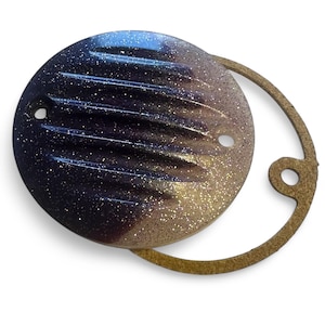 Puede incluir: Una tapa de motor redonda, metálica, púrpura y blanca, brillante, con una junta de goma marrón.