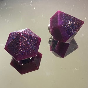 Peut inclure: Deux boucles d'oreilles en forme de diamant en résine, de couleur violette et scintillante. Les boucles d'oreilles sont facettées et ont un reflet métallique.