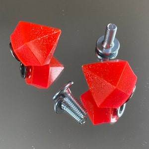 Peut inclure: Quatre pièces en résine de forme diamant rouge avec des attaches à vis en métal argenté. Les attaches ont une tête hexagonale et une base plate.