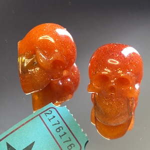 Puede incluir: Dos adornos de resina en forma de calavera de color naranja con purpurina. Las calaveras miden aproximadamente 5 cm de alto y tienen un acabado brillante y brillante.