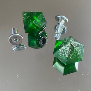 Peut inclure: Trois poignées de tiroir en forme de diamant vert avec des vis argentées. Les poignées ont une finition scintillante.