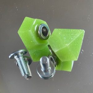 Peut inclure: Deux pièces de matériel de skateboard en forme de diamant vert avec des vis et des rondelles en métal argenté.