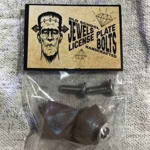 Peut inclure: Deux boulons de plaque d'immatriculation en forme de diamant gris avec une vis et une rondelle argentées. Les boulons sont emballés dans un sac en plastique transparent avec une étiquette qui indique "Old School Jewels Plate License Bolts Handcrafted".