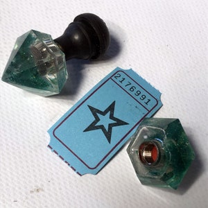 May include: Two green glass bottle stoppers with a star-shaped ticket with the number 2176991 printed on it.