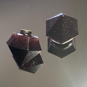 May include: Two black, geometric bottle stoppers with a glittery finish. The stoppers are shaped like a diamond and a hexagon.