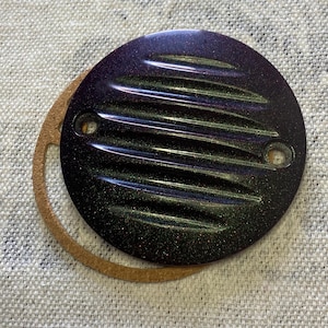 May include: A round, black, and green motorcycle engine cover with a ribbed design and a sparkly finish. The cover has two holes for mounting.