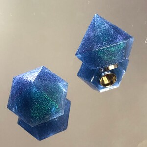 Può includere: Due forme geometriche in resina blu iridescente con un inserto filettato in oro metallico su una delle forme.