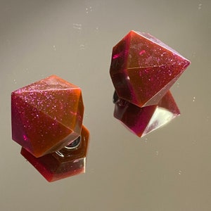 Puede incluir: Un par de pendientes de color rojo oscuro y marrón con purpurina en forma de diamante. Los pendientes están hechos de resina y tienen un acabado brillante.
