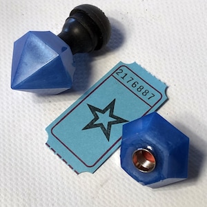 May include: A blue, geometric-shaped stamp with a black handle and a blue, geometric-shaped nut. A light blue ticket with a star graphic and the number 2176887 is also present.