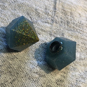 May include: Two geometric resin shapes, one with gold glitter and one with blue glitter. Both shapes have a hole in the top.